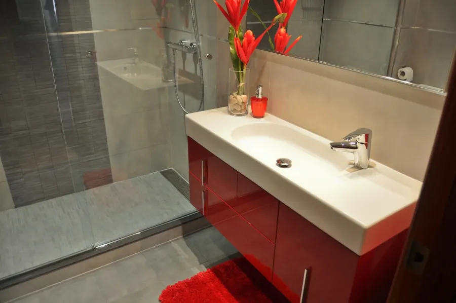 Baño con mueble de lavabo rojo y ducha con mampara de cristal