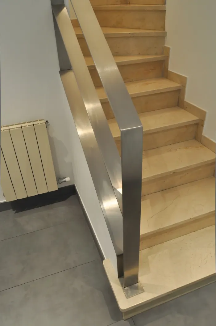 Escalera interior con peldaños de piedra clara y barandilla de acero